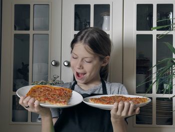 A young boy in an apron holds in his hands and demonstrates a pizza cooked at home 