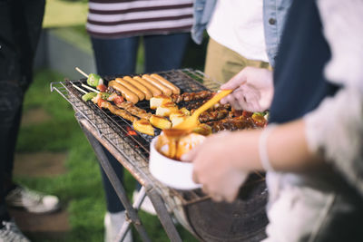 Midsection of people standing by barbecue grill at yard