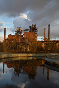 Reflection of factory on lake against sky