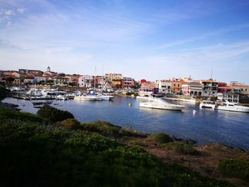 Sailboats moored in harbor by town against sky