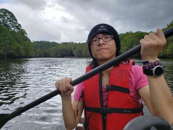 Portrait of young man rowing while sitting in boat against lake