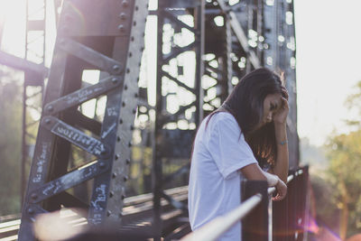 Sad young woman looking away while standing on bridge