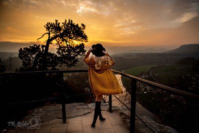 Woman standing by railing against sky during sunset