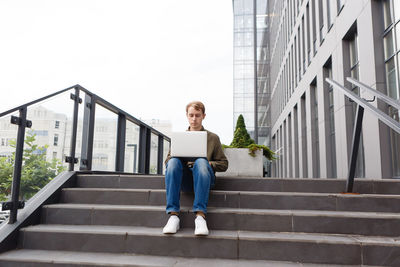 Man working on laptop sitting on the stairs of business center