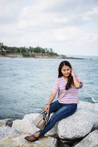 Portrait of smiling young woman sitting against sea