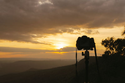 Silhouette of camera against sky during sunset