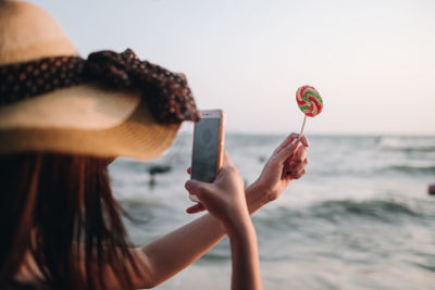 Close-up of woman photographing lollipop at beach against sky