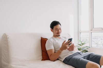 Young woman using mobile phone while sitting on bed at home