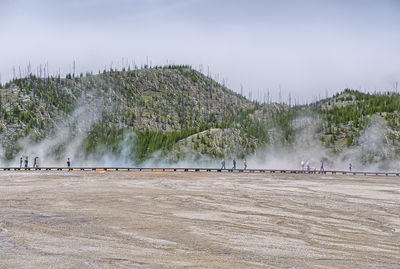 People on boardwalk by hot springs and mountains against sky