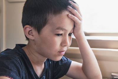 Close-up portrait of young asian thinking boy with hand to forehead