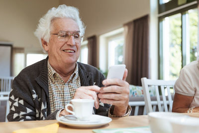 Senior man using mobile phone at breakfast table in nursing home