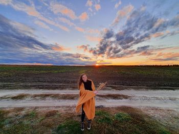 Woman standing on beach against sky during sunset