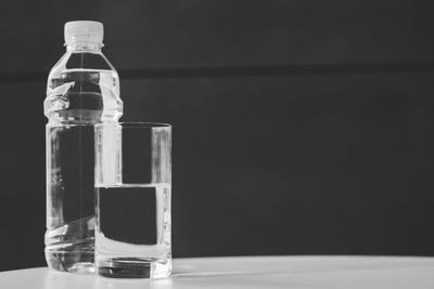 Close-up of drinking glass with water bottle on table against black background