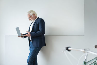 Businessman holding laptop by wall at office