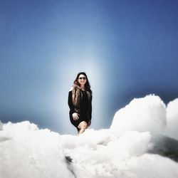 Portrait of smiling woman standing on snow against sky during sunny day