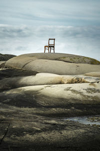 Chair on rock formation against cloudy sky