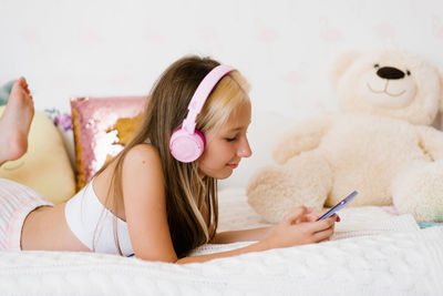 Beautiful teenage girl is relaxing in bed using a touchscreen smartphone, listening to music