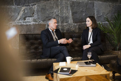 Businessman gesturing while discussing with female entrepreneur sitting on sofa at seminar