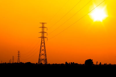 Silhouette electricity pylon against orange sky