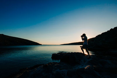 Man standing on rock at lakeshore against sky during sunset