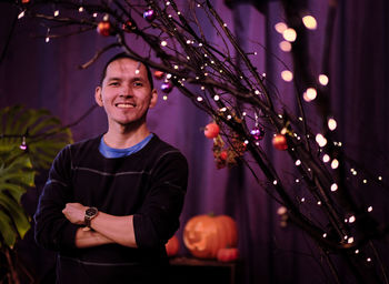 Portrait of smiling young man standing by illuminated decoration at night