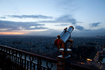 Coin-operated binocular at observation point by cityscape against sky during sunset