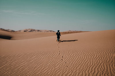 Rear view of man walking on sand at desert against clear sky
