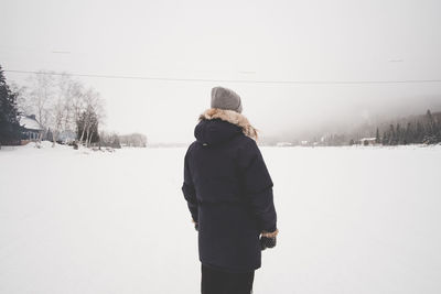 Rear view of woman standing on snow covered field against sky