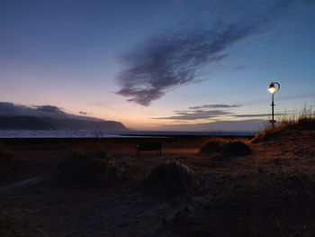 Street light on beach against sky at sunset