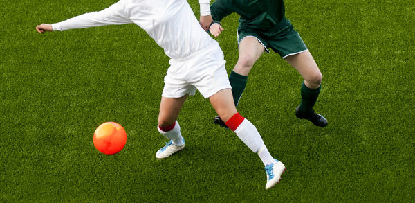 Low section of people playing soccer ball on grass