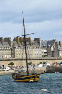 Sailboats in river by buildings in city against sky