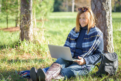 Mature woman using laptop while sitting on field in park