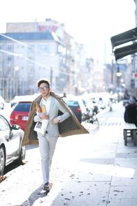 Man wearing jacket walking on sidewalk at city street holding bread in bag