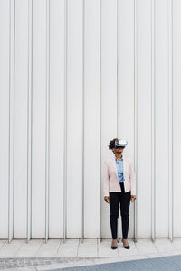 Businesswoman wearing virtual reality simulator in front of white wall