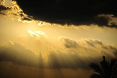 Low angle view of sunlight streaming through clouds during sunset