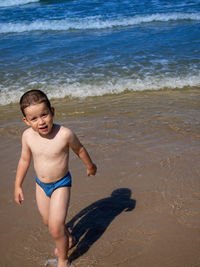 Young happy boy running and looking at camera on the beach during sunny summer day