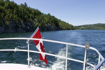 Boat sailing on lake against clear sky with canadian flag 