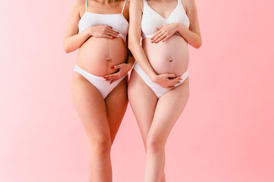 Midsection of woman wearing lingerie while standing against pink background