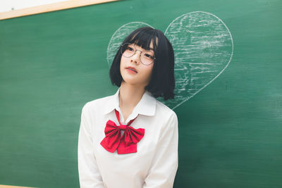 Portrait of beautiful young woman standing against green background