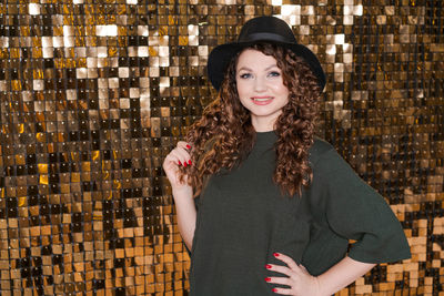 Beautiful young woman in black hat on background shiny golden wall, smiles