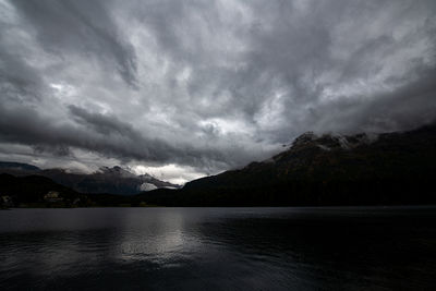 Scenic view of lake and mountains against storm clouds