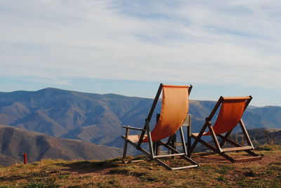 Deck chairs on land against sky