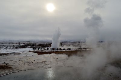 People at strokkur geyser erupting against sky