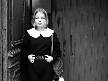 Portrait of young woman standing against door