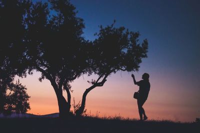 Silhouette man standing on field against sky during sunset