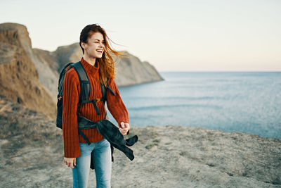 Beautiful young woman standing at beach against sky