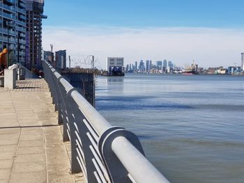 Bridge over river by buildings in city against sky