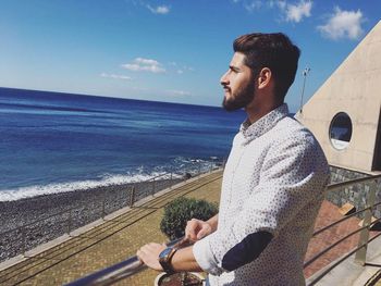 Side view of handsome man looking towards sea from walkway during sunny day