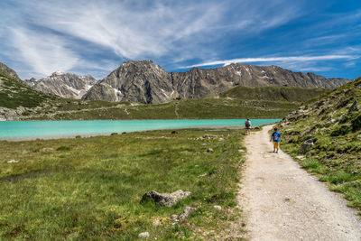 Rear view of woman and boy walking on dirt road against mountain