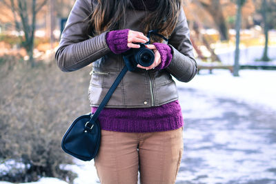 Midsection woman holding camera while standing on snow covered field